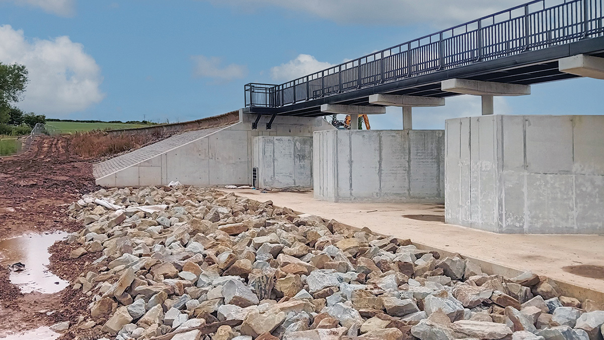 Footbridge over newly built spillway and riprap erosion protection upstream of concrete apron and labyrinth weir - Courtesy of Kier